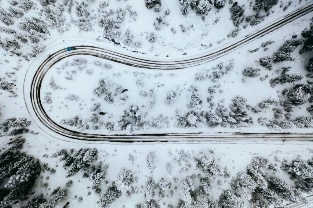 Photo of a winding road through snow and trees taken from an aerial view.